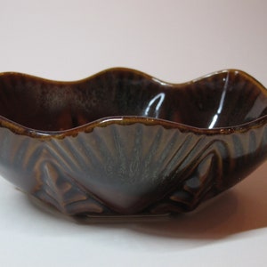 Könnte beinhalten: Eine braune Keramikschale mit einem welligen Rand und einem gewellten Design. Die Schale hat eine dunkelbraune Glasur mit einem dezenten Grünton.