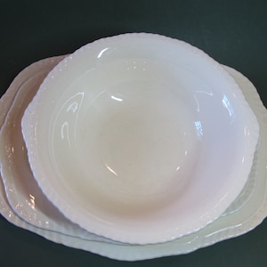 Puede incluir: Una pila de tres platos de cerámica blanca. Los dos inferiores son platos con un borde festoneado y un borde con cuentas. El plato superior es un cuenco con un borde festoneado similar. Los platos están sobre una superficie verde oscuro.