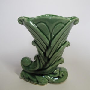 Peut inclure: Un vase en céramique vert avec un design unique et stylisé. Le vase a la forme d'une corne avec une large ouverture et une base étroite. La surface est décorée de lignes et de courbes en relief.