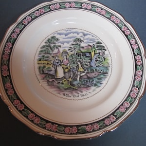 Peut inclure: Une assiette en céramique blanche avec un bord doré et une bordure florale noire et verte. Au centre de l'assiette, une illustration colorée d'un moulin avec des personnes et une rivière. Le texte "The Old Mill" est imprimé sous l'illustration.
