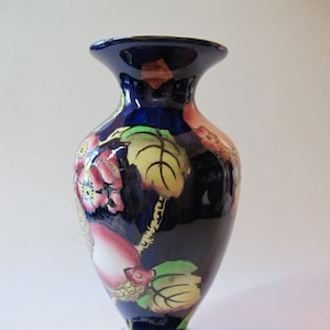 May include: A blue ceramic vase with a floral design. The vase has a wide mouth and a narrow base. The flowers are painted in shades of pink, yellow, and green.