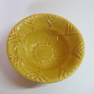 Op de afbeelding: Een gele keramische kom met een decoratief ontwerp van gestileerde bladeren. De kom heeft een licht afgeronde vorm en een gladde, glanzende afwerking.