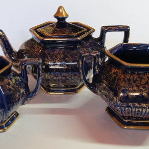 May include: A cobalt blue teapot, creamer and sugar bowl set with gold accents and floral patterns.