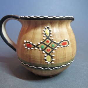 Può includere: Un'anfora in ceramica marrone con manico nero e bordatura bianca e nera. L'anfora presenta un disegno geometrico con accenti rossi, verdi, gialli e bianchi.