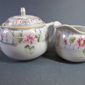 Peut inclure: Un ensemble sucrier et crémier en porcelaine vintage avec un motif floral. L'ensemble présente des fleurs roses avec des feuilles vertes sur un fond blanc avec des accents bleus et dorés.
