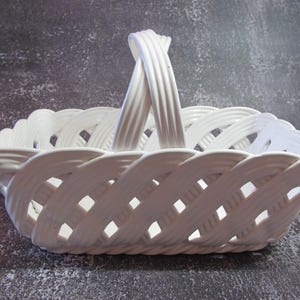 May include: White ceramic basket with a woven design and a handle. The basket is empty.