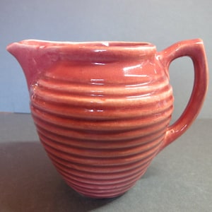 Può includere: Un creamer in ceramica rosa con un design a coste e un manico.