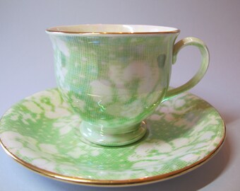 May include: A green and white teacup and saucer set with a gold rim. The teacup and saucer have a marbled pattern.