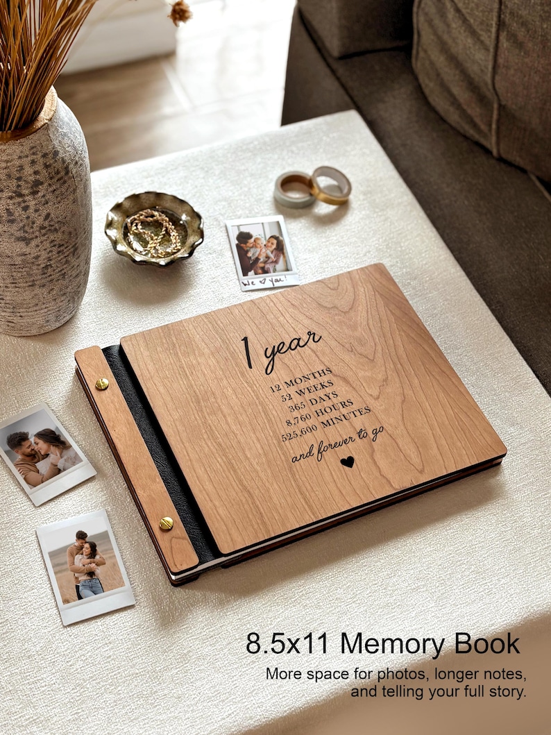 May include: A wooden memory book with the text "1 year" and related time measurements. The book is 8.5 x 11 inches and has a black spine. The image also shows several small photos, a decorative bowl, and some washi tape.