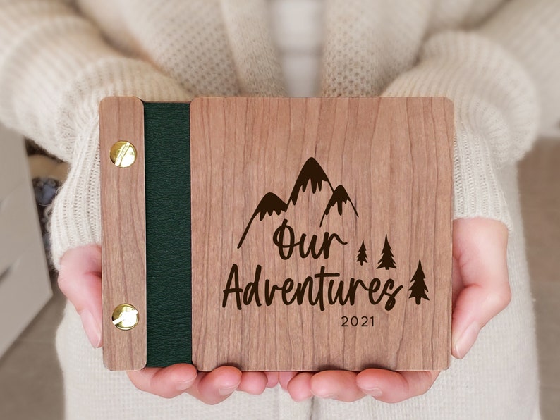 Mountain and forest scene engraved on a wooden adventure mini photo album with green vegan leather binding detail and modern gold hardware.