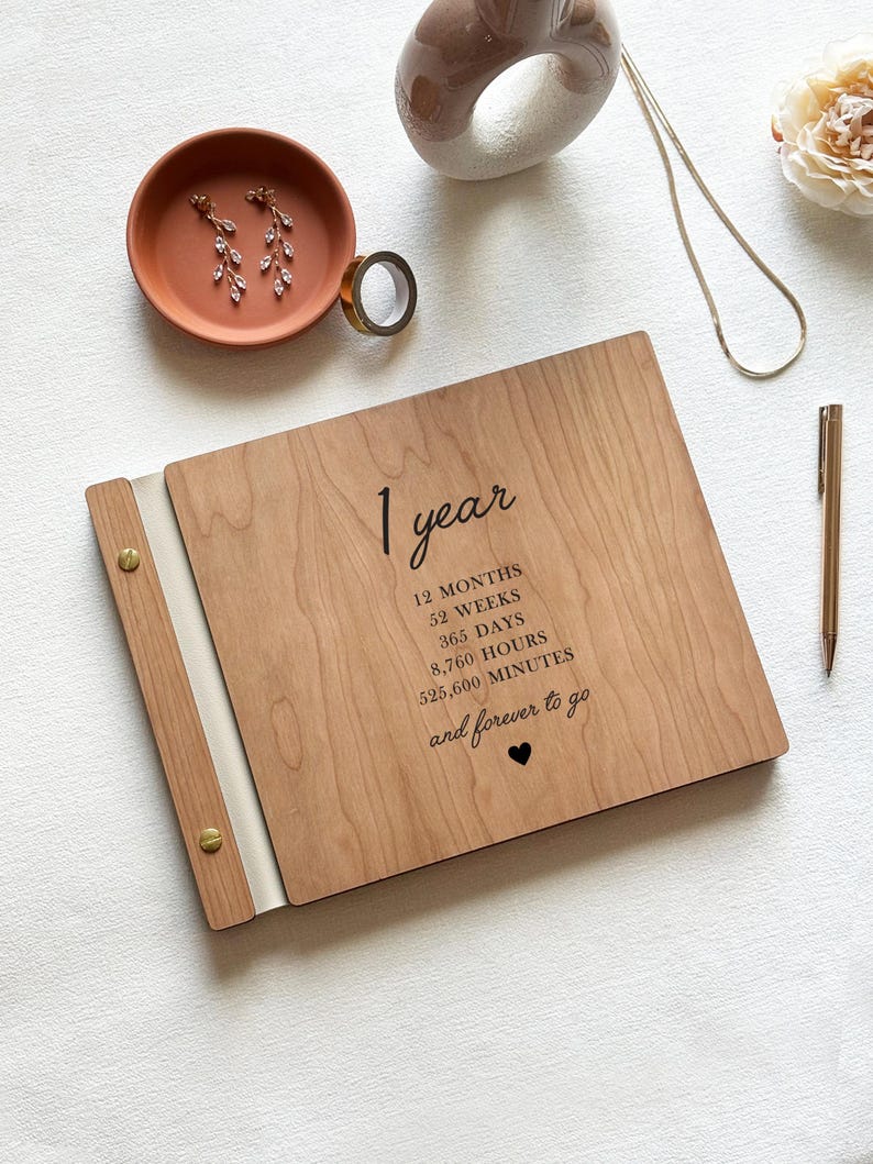 May include: A wooden anniversary keepsake with the text "1 year" and the time breakdown: 12 months, 52 weeks, 365 days, 8,760 hours, and 525,600 minutes. The phrase "and forever to go" is also included. A pen, earrings, and a decorative ring are also visible.