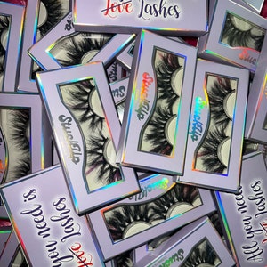 May include: A pile of purple boxes with the text "Stuck Up Cosmetics" and "All you need is Love Lashes" on them. The boxes contain false eyelashes.