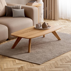Peut inclure: Un salon moderne avec un canapé sectionnel marron clair, des coussins beiges et des coussins décoratifs. Une table basse en bois repose sur un tapis gris, avec des objets décoratifs. La pièce a un parquet et des rideaux aux tons neutres.