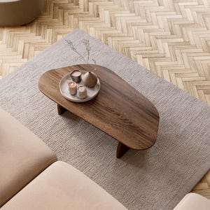 May include: An overhead shot of a living room setup featuring a dark wood coffee table with a decorative tray, a light gray rug, and a beige sofa. The table holds small candles and a vase. The floor is a light wood parquet.