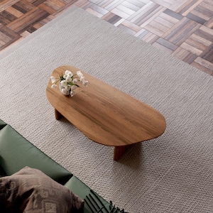 K&ouml;nnte beinhalten: Ein Couchtisch aus hellem Holz mit organischer, asymmetrischer Form. Der Tisch hat eine glatte, polierte Oberfl&auml;che und steht auf einem wei&szlig;en Teppich. Ein kleiner Strau&szlig; wei&szlig;er Blumen steht auf dem Tisch.