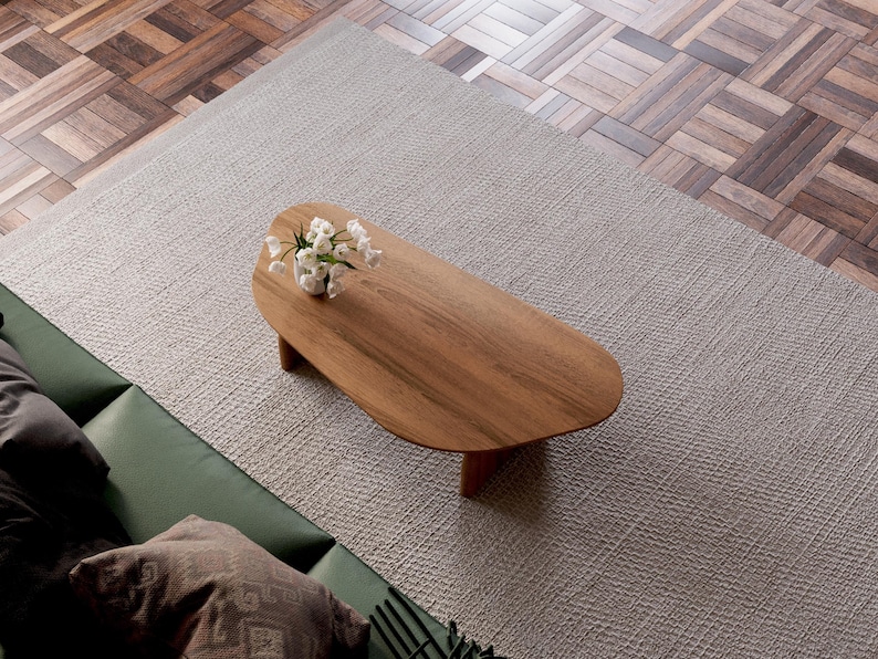 K&ouml;nnte beinhalten: Ein Couchtisch aus hellem Holz mit organischer, asymmetrischer Form. Der Tisch hat eine glatte, polierte Oberfl&auml;che und steht auf einem wei&szlig;en Teppich. Ein kleiner Strau&szlig; wei&szlig;er Blumen steht auf dem Tisch.