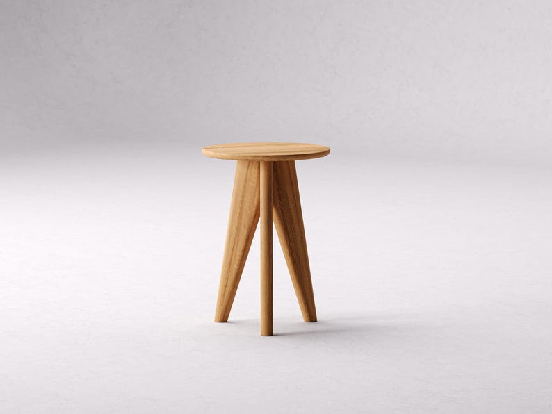 May include: A wooden side table with a round top and three legs. The table is made of light brown wood and has a simple design.