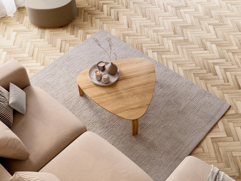 May include: An overhead shot of a living room setup featuring a light brown, heart-shaped wooden coffee table on a gray rug. The table holds a tray with small decorative items. A beige sectional sofa and a round ottoman are also visible.