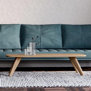 May include: A teal sofa with a wooden coffee table and a decorative rug. The coffee table has a light wood finish and a unique angled leg design. Clear glass vases with dark stems sit on the table.