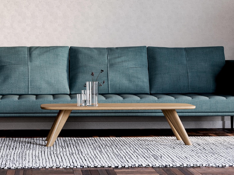 May include: A teal sofa with a wooden coffee table and a decorative rug. The coffee table has a light wood finish and a unique angled leg design. Clear glass vases with dark stems sit on the table.
