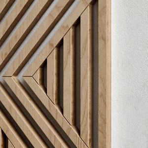 May include: A wooden wall panel with a geometric design of overlapping lines creating a triangular pattern. The panel is made of light brown wood with a natural grain.
