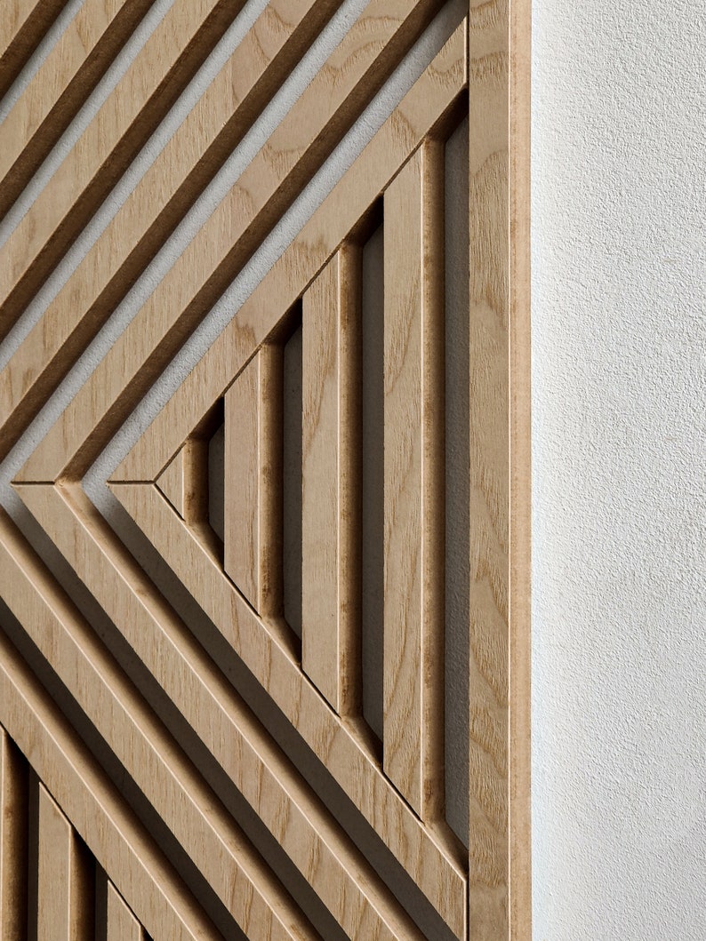 May include: A wooden wall panel with a geometric design of overlapping lines creating a triangular pattern. The panel is made of light brown wood with a natural grain.