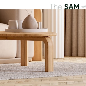 May include: A light wood coffee table with rounded edges and curved legs. The table supports a white tray with white cups and a decorative vase. The text "The SAM coffee table" is in the upper right corner. The table sits on a gray rug.