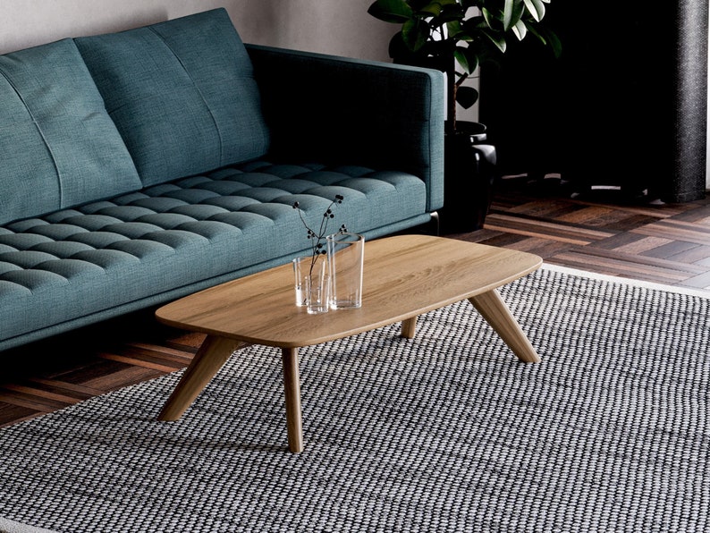 May include: A modern living room scene featuring a wooden coffee table with angled legs. The table is positioned in front of a teal sofa and a patterned rug. Clear glass vases with stems are on the table.