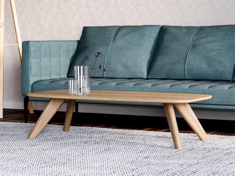 May include: A light oak coffee table with angled legs sits on a white and gray patterned rug. A teal sofa is in the background. Clear glass vases with a sprig of berries are on the table. Modern living room furniture.