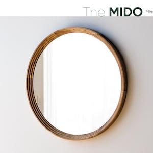 May include: A round mirror with a light brown wooden frame. The frame has a layered design. The mirror is hanging on a white wall. The text "The Mido Mirror" is at the top.
