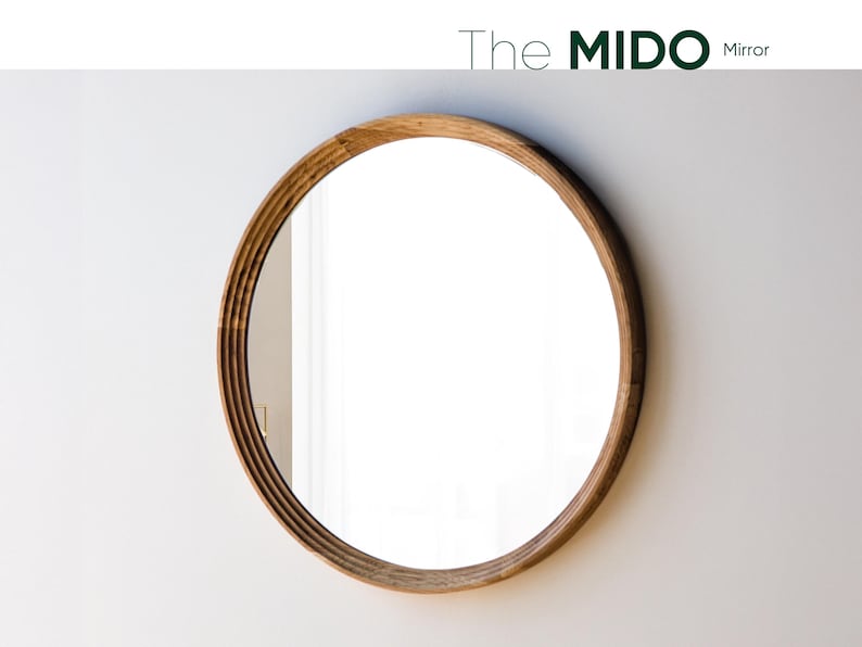 May include: A round mirror with a light brown wooden frame. The frame has a layered design. The mirror is hanging on a white wall. The text "The Mido Mirror" is at the top.