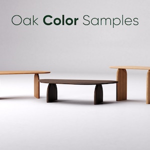 Op de afbeelding: Drie houten tafels in verschillende eiken kleuren. De tafels hebben een minimalistisch ontwerp met afgeronde bladen en gebogen poten. De tekst "Oak Color Samples" staat boven de tafels.