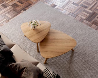 May include: Two wooden triangle-shaped coffee tables with a light wood finish. The tables are nested together on a light gray rug.