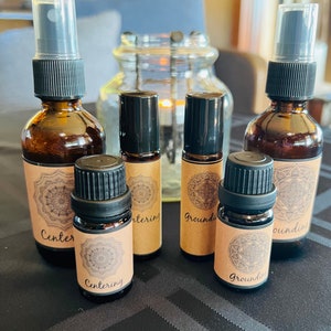 May include: Six essential oil bottles with brown glass and black caps. The bottles are labeled with the words "Centering" and "Grounding".