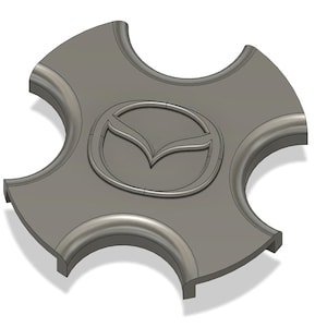 Könnte beinhalten: Graue Radkappe in Kleeblattform mit Mazda-Logo in der Mitte. Das Logo ist ein stilisiertes Flügeldesign in einem Kreis. Die Radkappe hat einen gebogenen, erhöhten Rand.