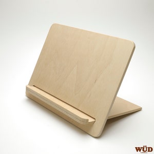 Op de afbeelding: Een boekenstandaard van licht hout met een schuin oppervlak en een klein plateau om een boek of tablet te houden.
