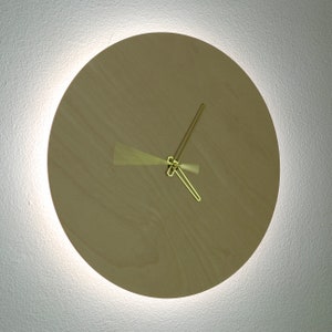 May include: A round, wooden clock with gold-colored hands. The clock is mounted on a white wall.