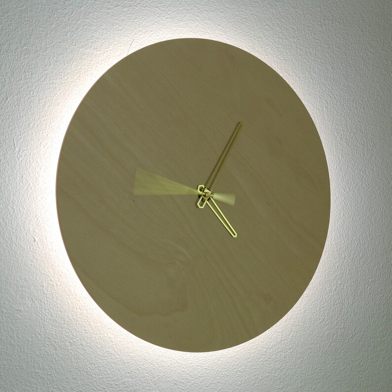 May include: A round, wooden clock with gold-colored hands. The clock is mounted on a white wall.