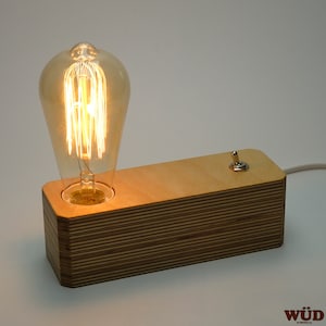 May include: A wooden table lamp with a light bulb and a switch. The lamp is made of plywood and has a natural wood finish.