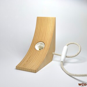 May include: A wooden lamp base with a white cord and a white light socket. The base is made of light wood and has a curved shape.