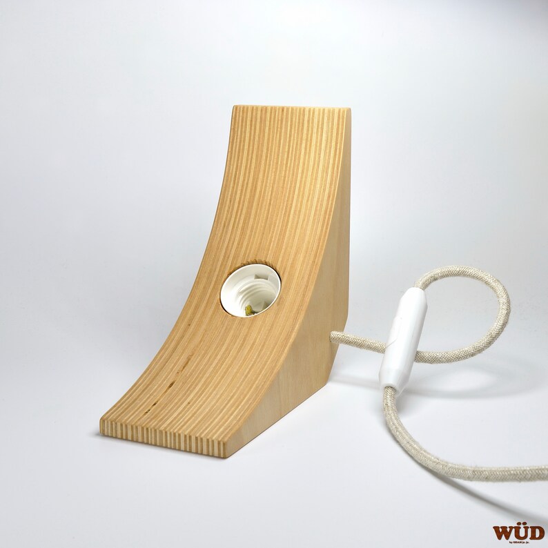 May include: A wooden lamp base with a white cord and a white light socket. The base is made of light wood and has a curved shape.