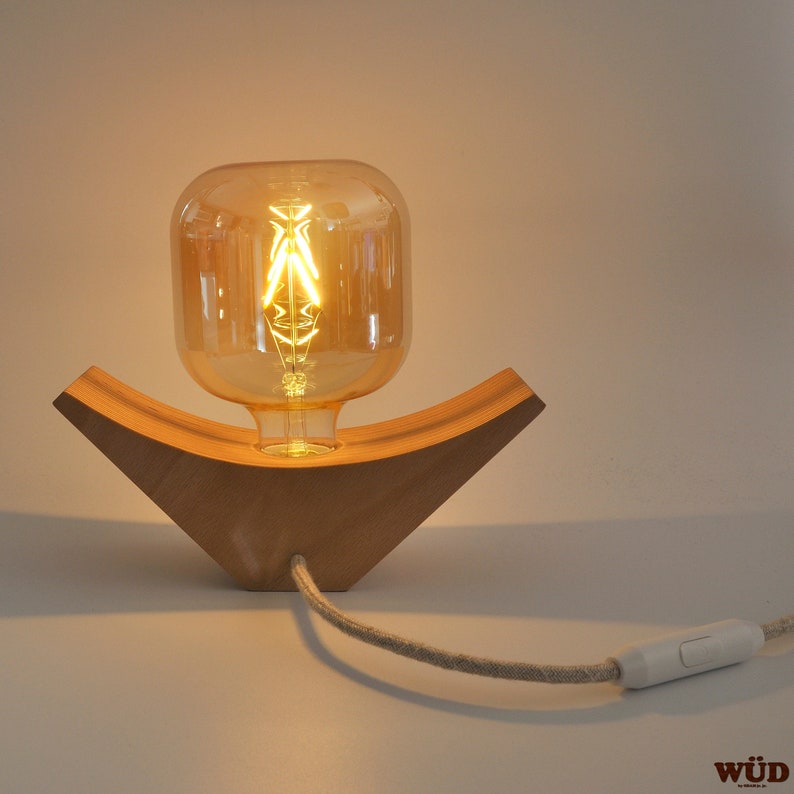 May include: A wooden table lamp with a curved base and a clear glass bulb with a filament. The lamp has a white cord with a switch.