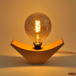 May include: A wooden table lamp with a warm, glowing light bulb. The lamp base is shaped like a crescent moon and is made of light wood.