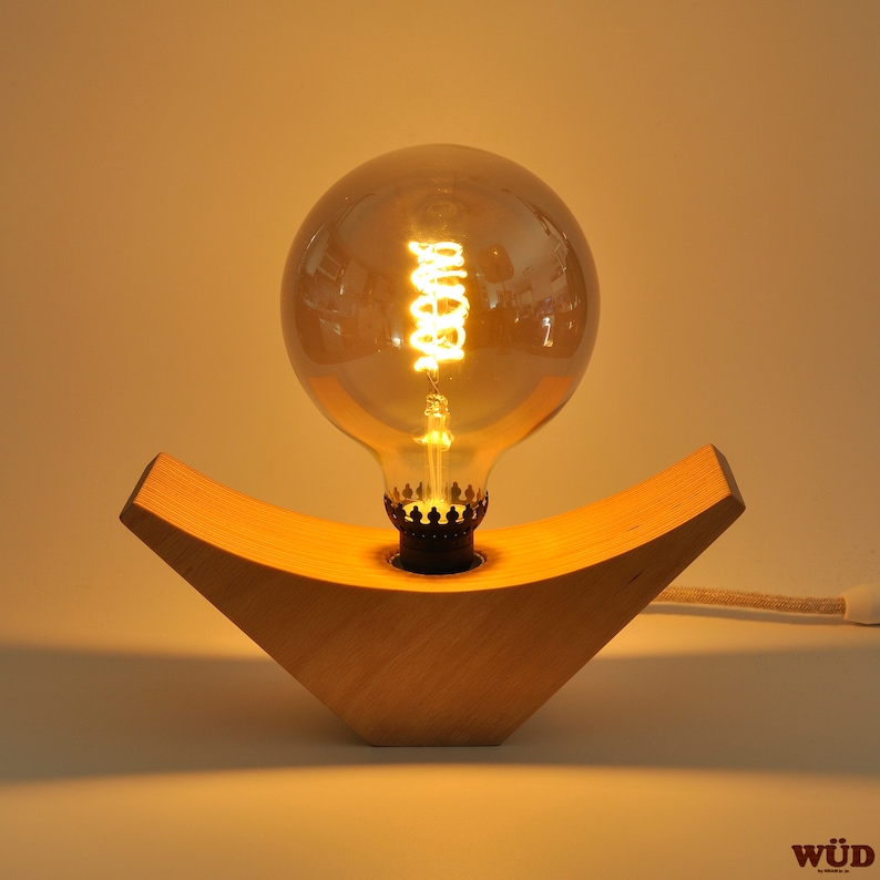 May include: A wooden table lamp with a warm, glowing light bulb. The lamp base is shaped like a crescent moon and is made of light wood.