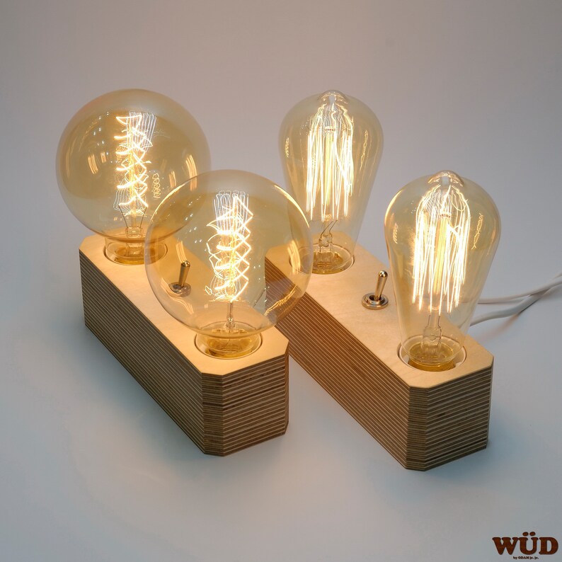 May include: Two wooden light fixtures, each with two vintage-style Edison light bulbs. The bulbs have a warm, amber glow and are set on a rectangular base. Each base has a toggle switch and a white power cord.