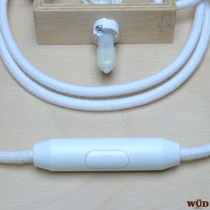 May include: White cord with a white inline switch and a white light bulb socket. The switch has a power symbol on it. The cord is coiled and the socket is attached to a wooden block with the word "W&Uuml;D" printed on it.