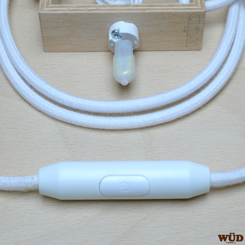 May include: White cord with a white inline switch and a white light bulb socket. The switch has a power symbol on it. The cord is coiled and the socket is attached to a wooden block with the word "W&Uuml;D" printed on it.