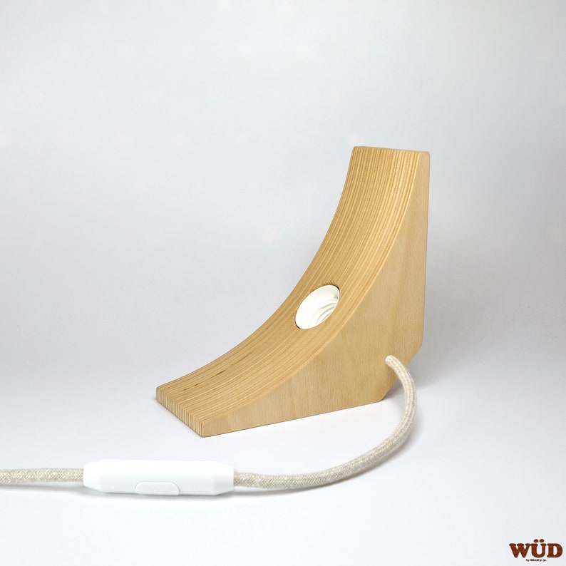 May include: A wooden lamp base with a curved design and a white cord with a switch. The lamp base has a white socket for a light bulb.