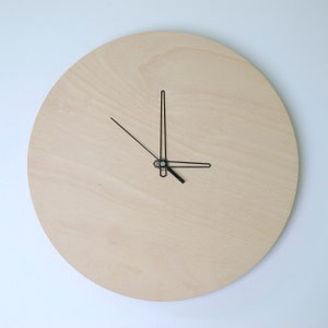 May include: A simple, minimalist clock with black hands on a light wood background.
