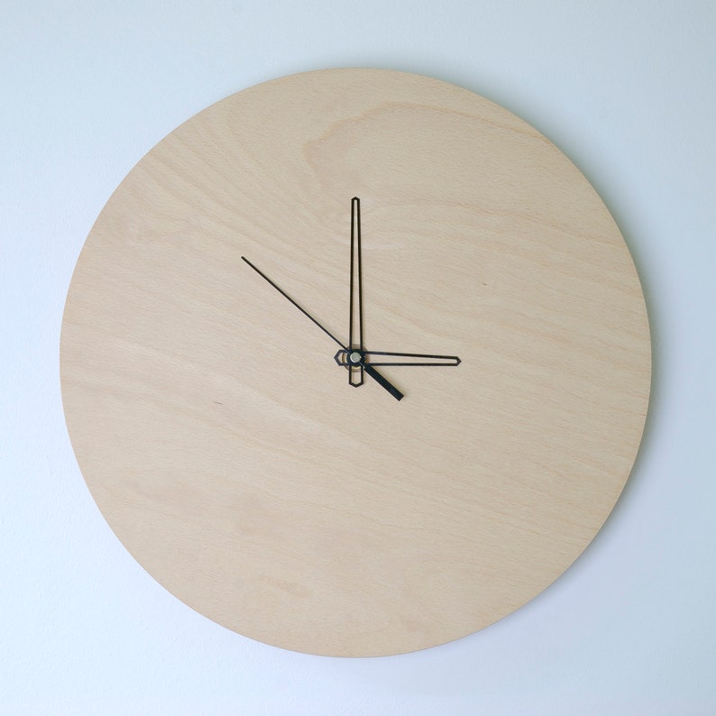 May include: A simple, minimalist clock with black hands on a light wood background.
